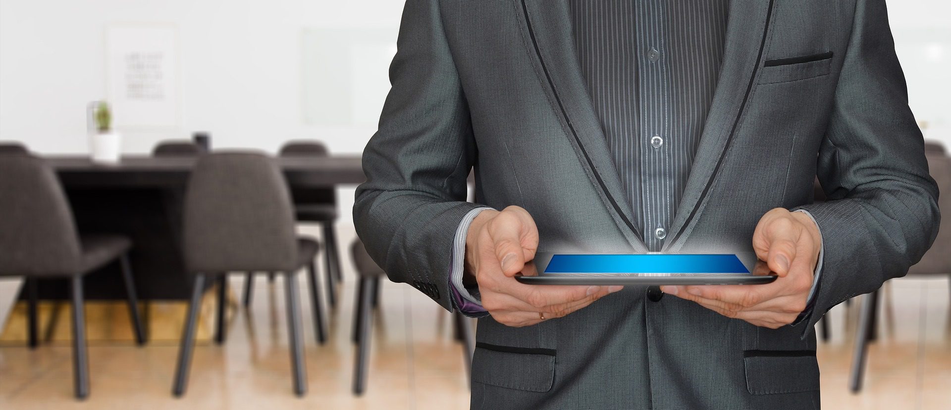Businessman (face not seen) holds iPad horizontally. It has a glowing blue screen.