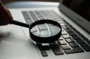 Magnifying glass held over a computer keyboard to denote staying focused when choosing domain names