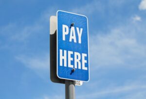 Blue 'Pay here' roadsign to illustrate the danger of hidden fees when buying a domain name.