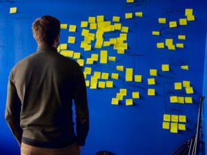 Man with back to camera stared at blue board full of yellow brainstorming notes