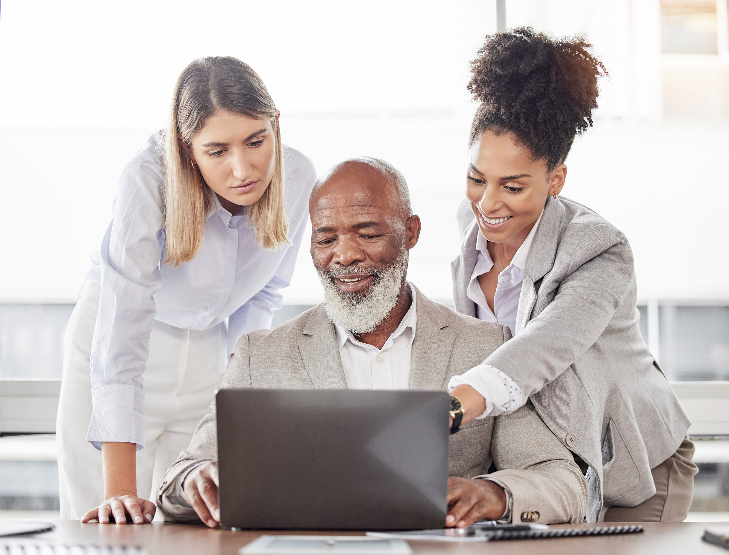 Two women, standing, and a man, seated, stare at a laptop screen