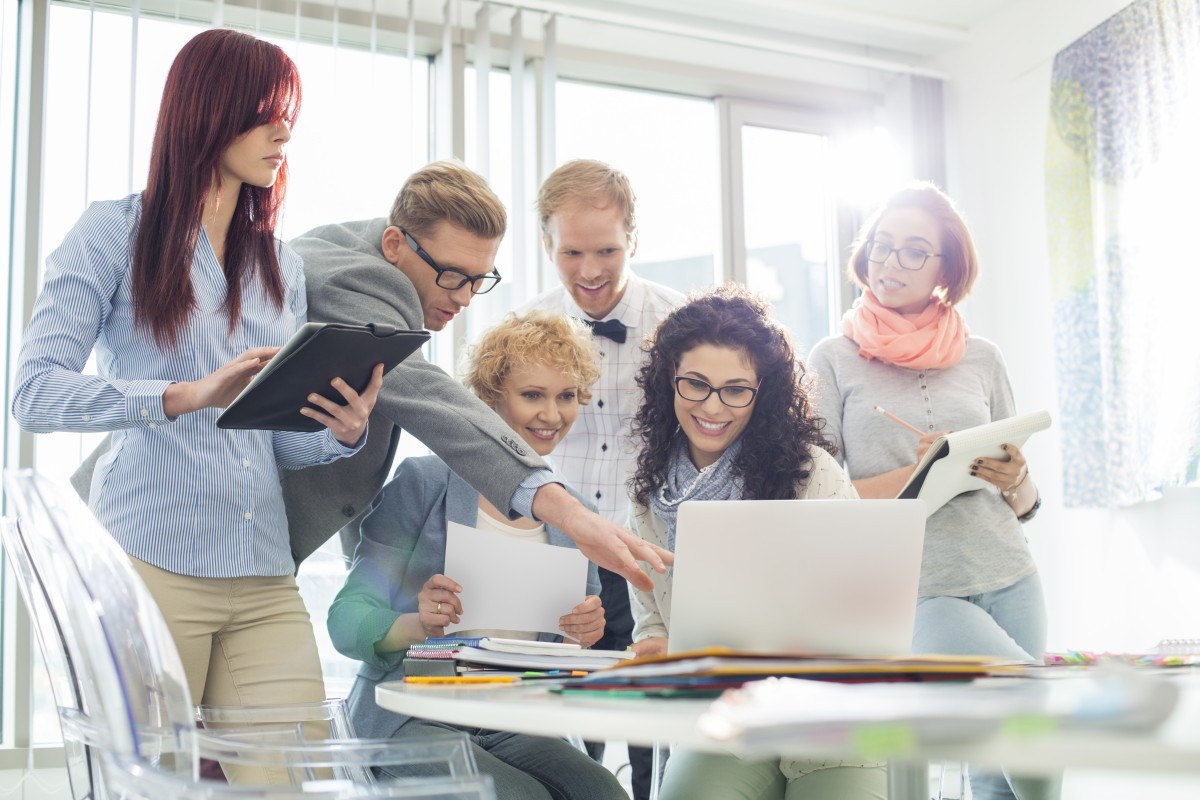 Family of people of various ages crowded around a computer as if investigating domain name services online.
