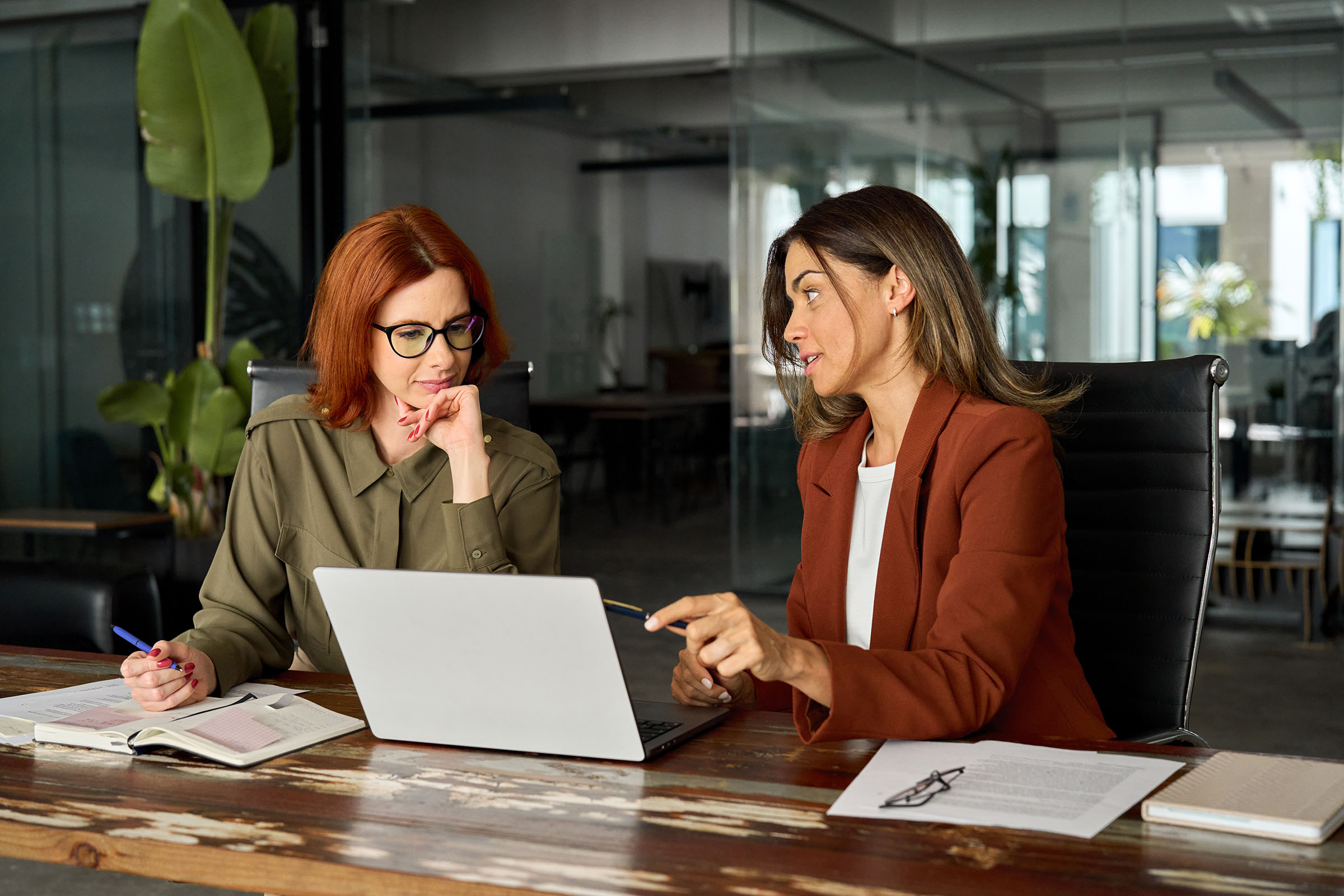 Two busy female co-workers sat next to each other looking at a laptop