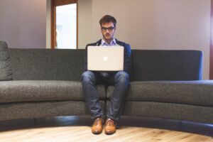 man sitting alone on sofa typing into laptop
