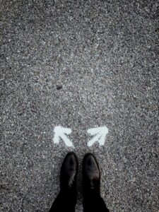 Looking down at two feet on a pavement with an arrow pointing left and one pointing right