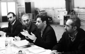Black and white image of four men at a business table, as if in mid-negotiation.